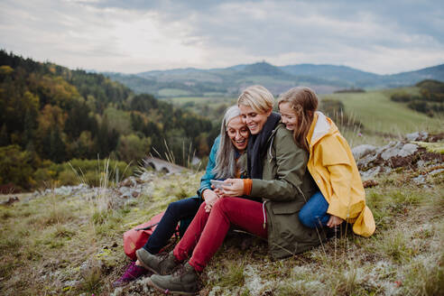 Ein kleines Mädchen mit Mutter und Großmutter, die auf dem Gipfel eines Berges ihr Smartphone überprüfen. - HPIF06055