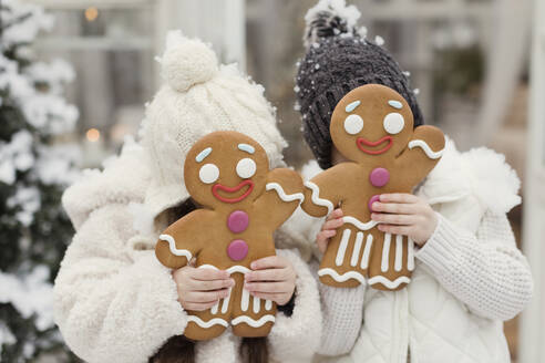 Sister and brother covering face with gingerbread man cookies - ONAF00374