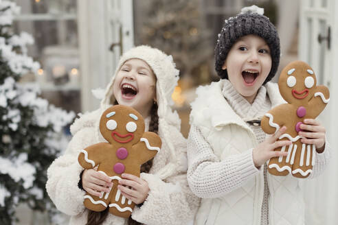 Happy children having fun with gingerbread man cookies outside house - ONAF00375