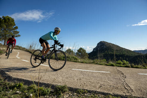 Cyclists riding bicycle on road under sky in sunlight - AMNF00112