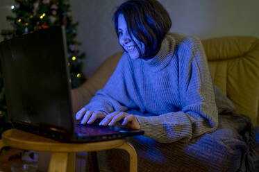 Frau sieht sich nachts im Wohnzimmer einen Film auf dem Laptop an - ANAF00833