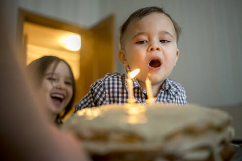 Junge bläst Kerzen auf Kuchen aus und feiert seinen Geburtstag zu Hause - ANAF00844