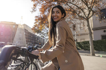 Smiling young woman renting bicycle on sunny day - JCCMF08939