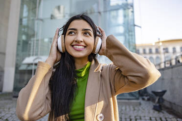 Nachdenkliche junge Frau mit Kopfhörern vor einem Gebäude - JCCMF08946