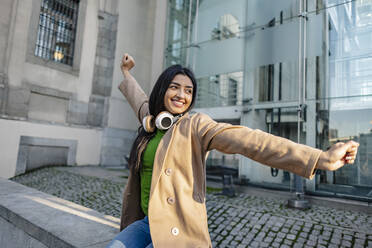 Happy young woman stretching arms outside building - JCCMF08947