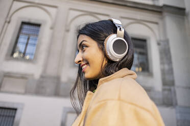 Kontemplative Frau mit Kopfhörern vor einem Gebäude - JCCMF08949