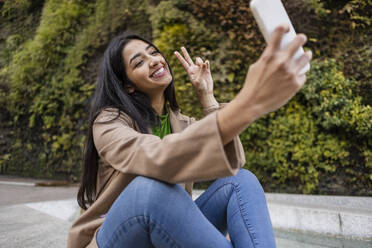Glückliche junge Frau nimmt Selfie durch Smartphone außerhalb vertikalen Garten - JCCMF08954