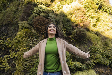 Carefree woman with arms outstretched outside vertical garden - JCCMF08955