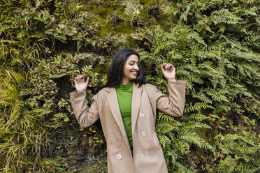 Happy young woman enjoying in front of hedge - JCCMF08957