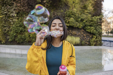 Young woman blowing bubbles at footpath - JCCMF08965