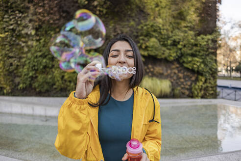 Young woman blowing bubbles at footpath - JCCMF08965