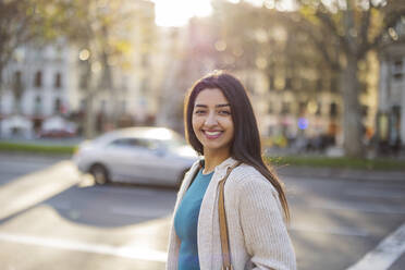 Smiling young woman standing at street on sunny day - JCCMF08985