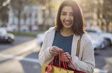 Glückliche junge Frau mit Einkaufstüten an einem sonnigen Tag - JCCMF08987
