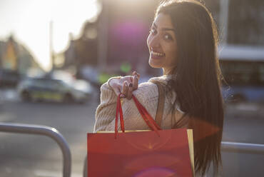 Happy young woman with shopping bag standing by railing - JCCMF08990