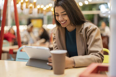 Happy woman using tablet PC sitting in cafe - JCCMF08995