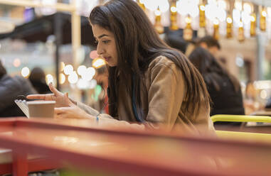 Frau mit In-Ear-Kopfhörern bei der Nutzung eines Tablet-PCs in einem Café - JCCMF08997