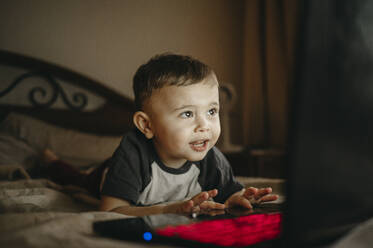 Junge mit Laptop auf dem Bett liegend zu Hause - ANAF00857