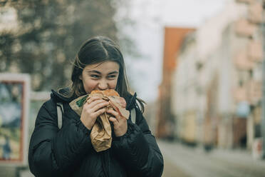 Teenage girl eating burger on street - VSNF00301