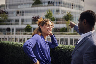 Businessman pointing by colleague leaning on plants - PWF00625