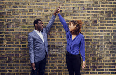 Business colleagues giving high-five to each other standing in front of wall - PWF00633