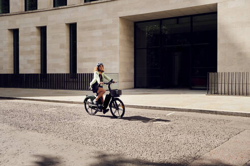 Businesswoman commuting through electric bicycle on road near building - PWF00640