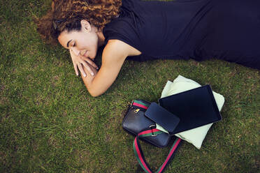 Smiling businesswoman lying by office stuff on grass at park - PWF00660