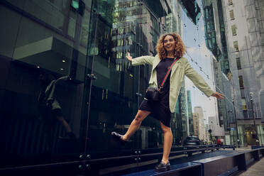 Happy businesswoman with arms outstretched balancing on bench near office building - PWF00666