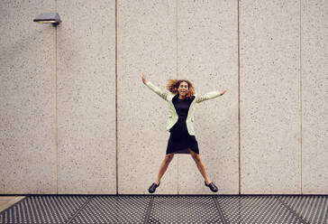 Fröhliche Geschäftsfrau, die vor eine Wand springt - PWF00670