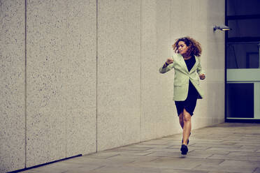 Businesswoman checking time and running on footpath near wall - PWF00672