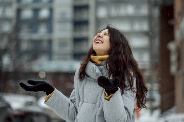 Happy woman wearing warm clothing enjoying snowfall - ANAF00860