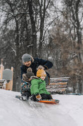 Vater und Jungen beim Schlittenfahren auf einem verschneiten Hügel - ANAF00868