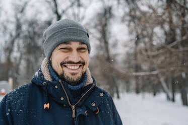 Happy man wearing knit hat enjoying snowfall - ANAF00871