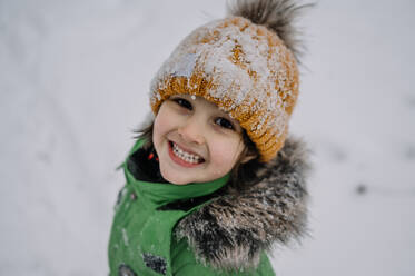 Niedlicher Junge mit Strickmütze spielt im Schnee - ANAF00873