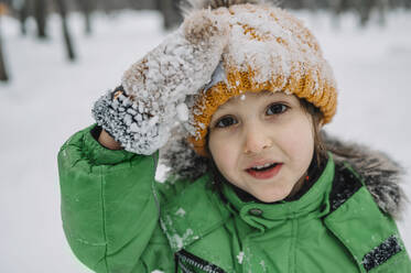 Unschuldiger Junge mit Strickmütze und Handschuhen, bedeckt mit Schnee - ANAF00874