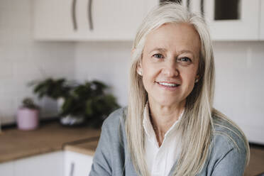 Happy mature woman with gray hair sitting at home - EBBF07641