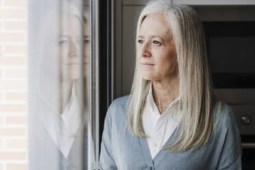Nachdenkliche reife Frau mit grauem Haar am Fenster zu Hause - EBBF07643