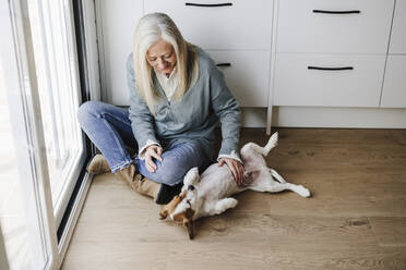 Reife Frau streichelt Hund auf dem Boden zu Hause - EBBF07645