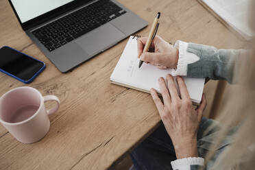 Hand of mature freelancer writing in diary with pen at home - EBBF07679