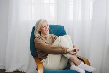 Happy mature woman sitting on armchair - EBBF07683