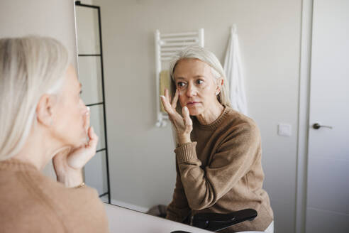 Frau trägt im Badezimmer Feuchtigkeitscreme auf das Gesicht auf - EBBF07711