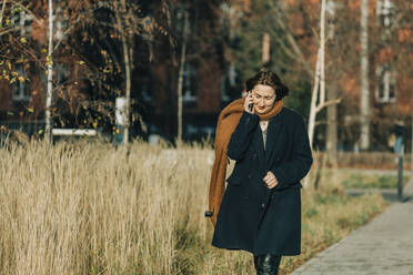 Ältere Frau, die mit ihrem Smartphone telefoniert und auf dem Fußweg spazieren geht - VSNF00302