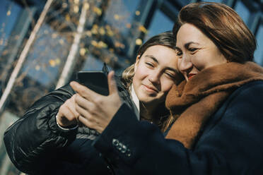 Lächelnde Mutter und Tochter benutzen ein Smartphone an einem sonnigen Tag - VSNF00303