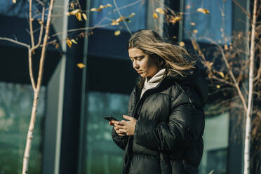 Teenage girl using smart phone in front of building - VSNF00304