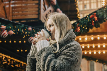 Blonde Frau trinkt Kaffee auf dem Weihnachtsmarkt - VSNF00316