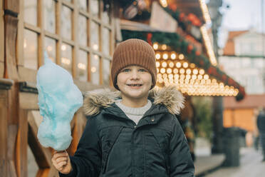 Glücklicher Junge mit Zuckerwatte auf dem Weihnachtsmarkt - VSNF00318