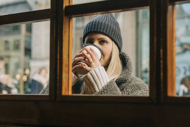 Woman drinking coffee seen through glass window - VSNF00319
