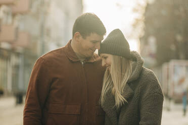 Smiling woman wearing knit hat embracing man - VSNF00323