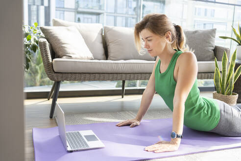 Frau beim Online-Yoga-Kurs mit Laptop auf dem Balkon - SVKF01041