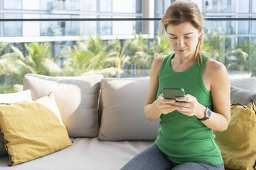 Frau surft auf dem Sofa sitzend auf dem Balkon mit ihrem Mobiltelefon im Internet - SVKF01051