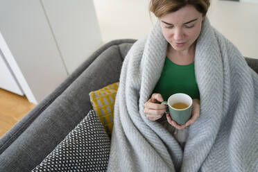 In eine Decke gewickelte Frau trinkt zu Hause Tee - SVKF01060